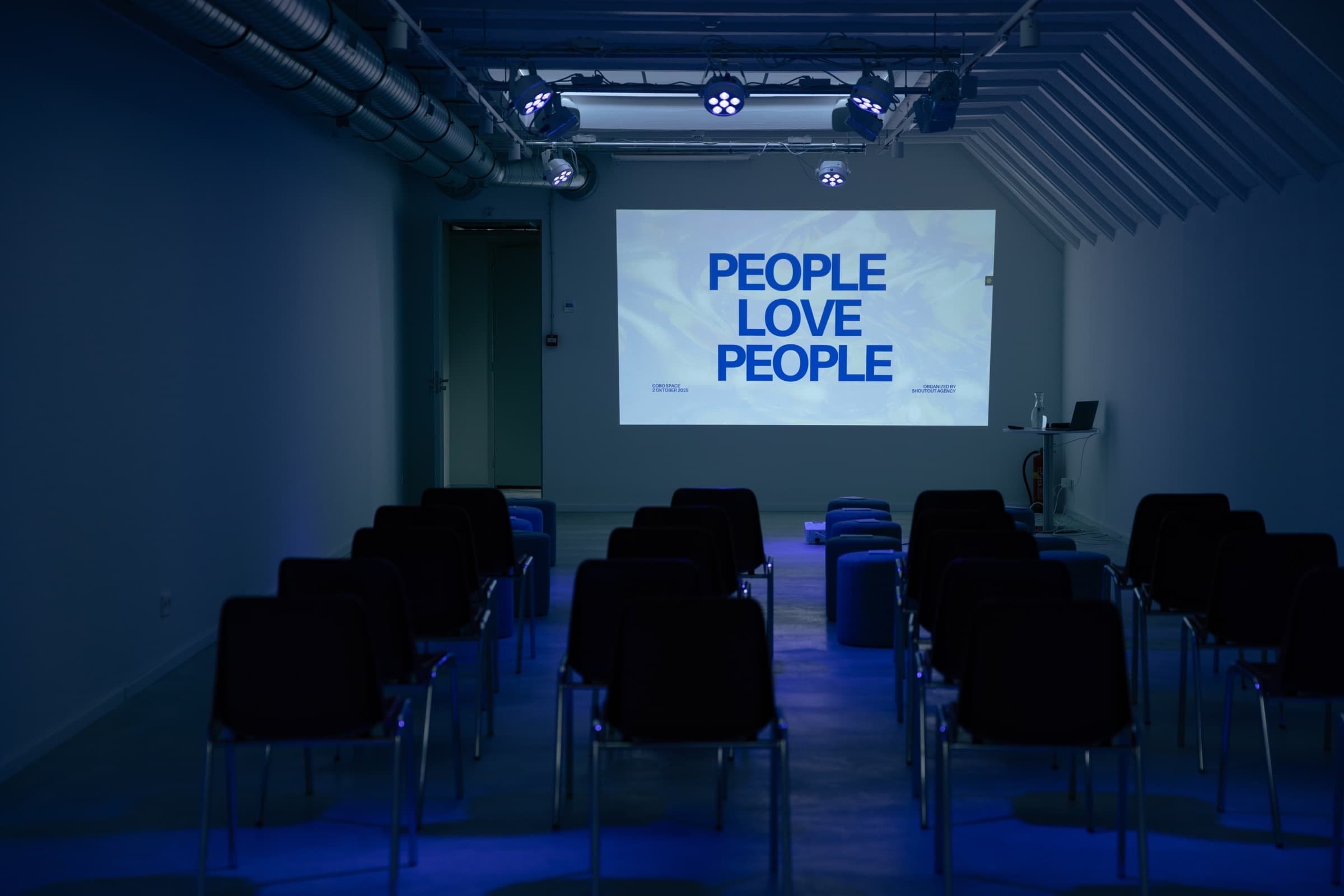 The talk room at COKO space: rows of chairs under blue stage lights facing a projection screen
